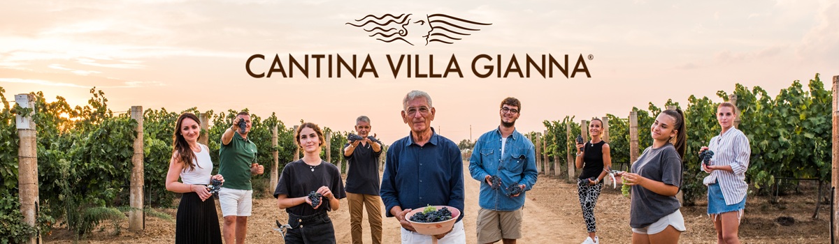 Group of people standing in a vineyard at sunset, holding grape clusters in front of a Cantina Villa Gianna banner.